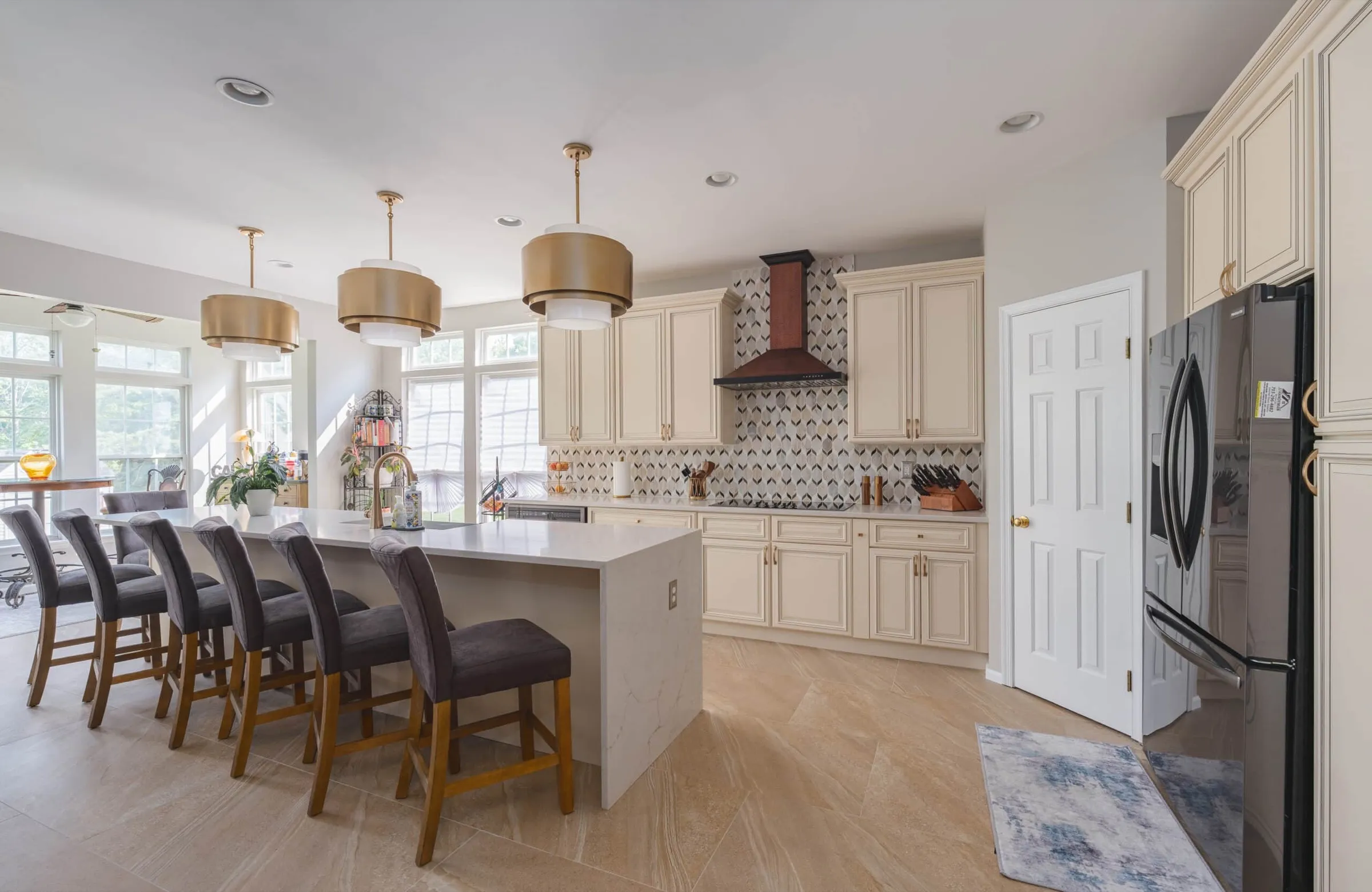 Remodeled open kitchen with cream cabinets, a long white island with dark stools and gold pendant lights